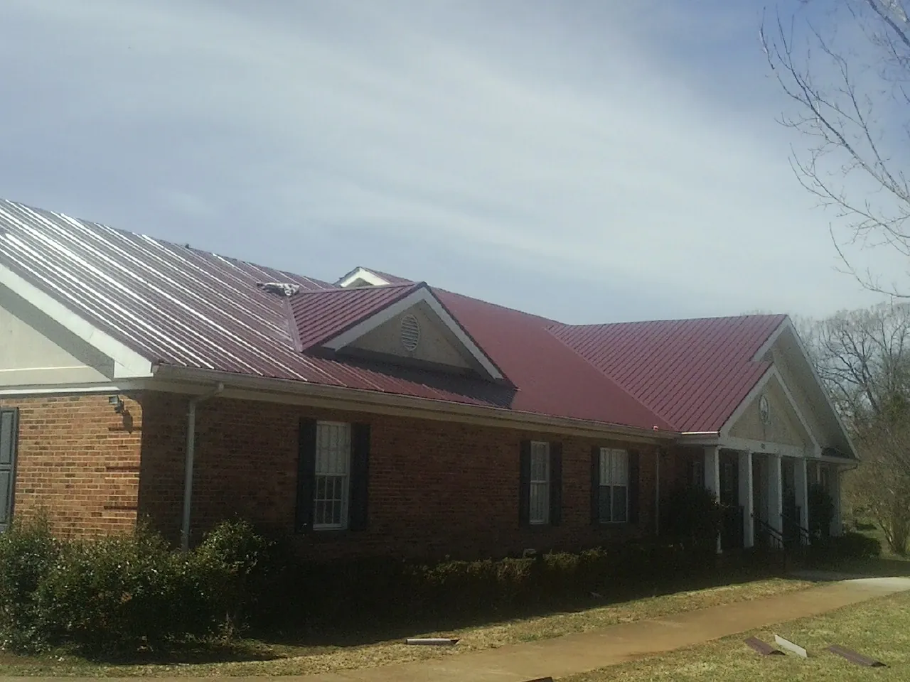 Red metal roof with gabled entries on a long brick building, from a Hail Damage Roof Repair job in Wayne