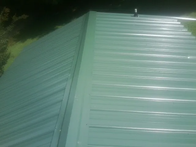 New green metal panels meeting at the ridge of a roof — Flat Roof Repair work by our crew in Wayne
