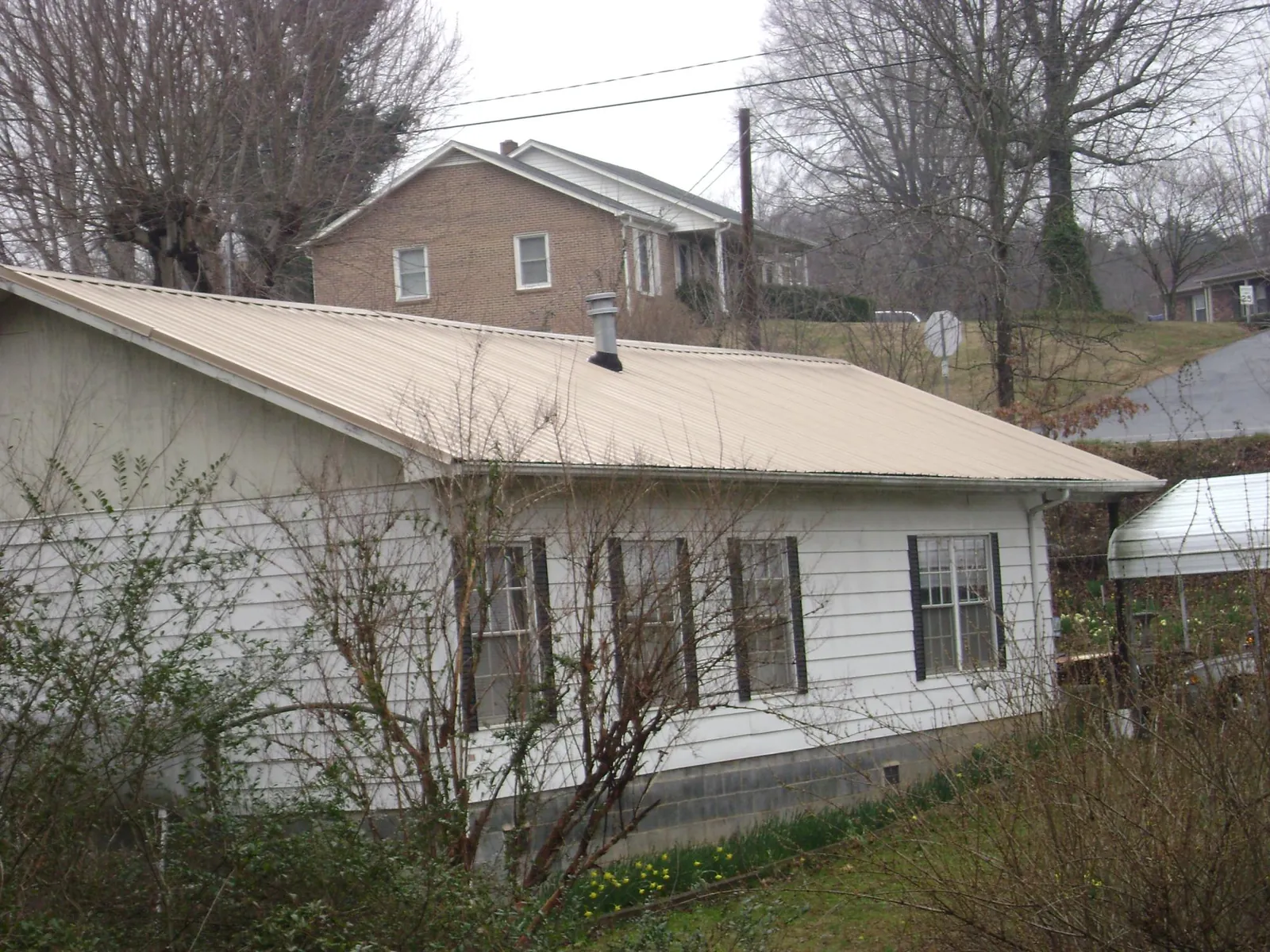 Tan metal roof on a white sided house set into a hillside — Commercial Roofing by Roofing Brothers in Wayne